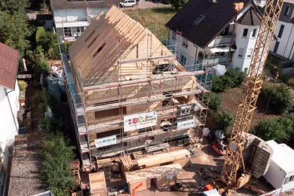 Holzhaus-Baustelle aus der Luft mit Kran und Gerüst Luftaufnahme einer Baustelle: Haus im Holzbau mit Gerüst und Dachkonstruktion, daneben ein Baukran.