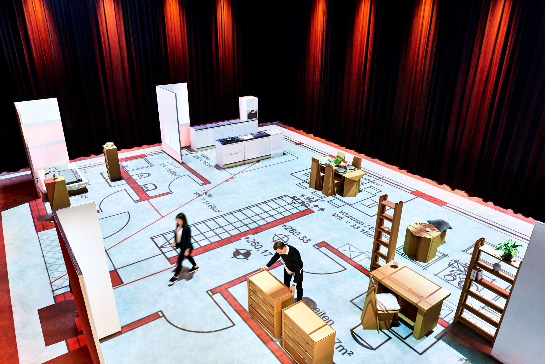 Begehbarer Grundriss als Projektion mit Möbel- und Wandmodulen Große Bodenprojektion eines Grundrisses; darauf stehen modulare Wände und Möbel, zwei Personen bewegen sich im Raum.