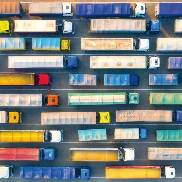 Vogelperspektive auf mehrere LKW in verschiedenen Farben auf einer mehrspurigen Straße.